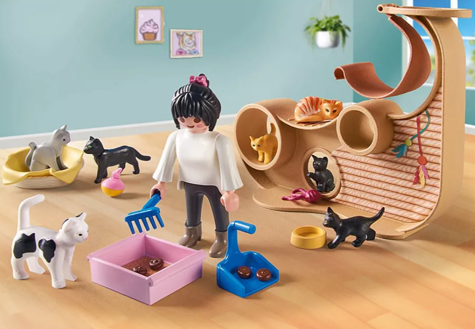 Eine Szene mit Katzenspielzeug und Figuren. Eine Person mit einer Harke steht in der Nähe einer Katzentoilette. Katzenfiguren sind in einem Katzenbaum.