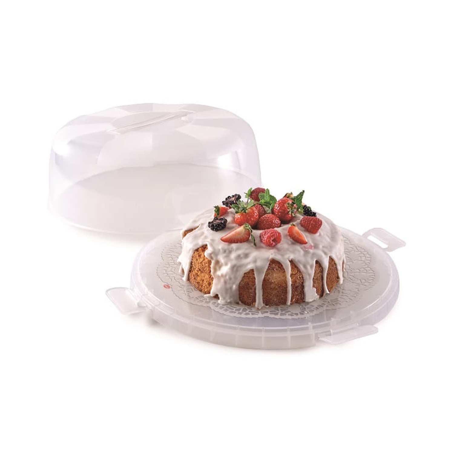 Una torta con glassa bianca e bacche è in un contenitore di plastica per torte, coperchio aperto. La torta è su un centrino di carta bianco.