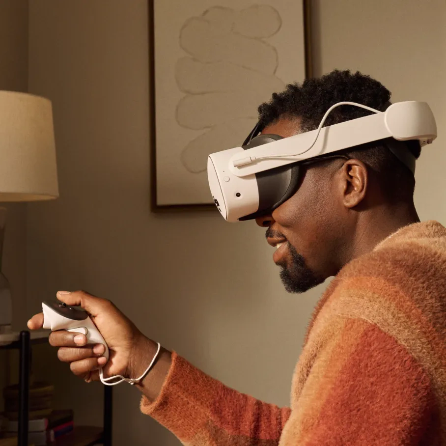 Mann mit VR-Headset und Controller. Er lächelt. Raum mit Lampe und Kunstwerk im Hintergrund.
