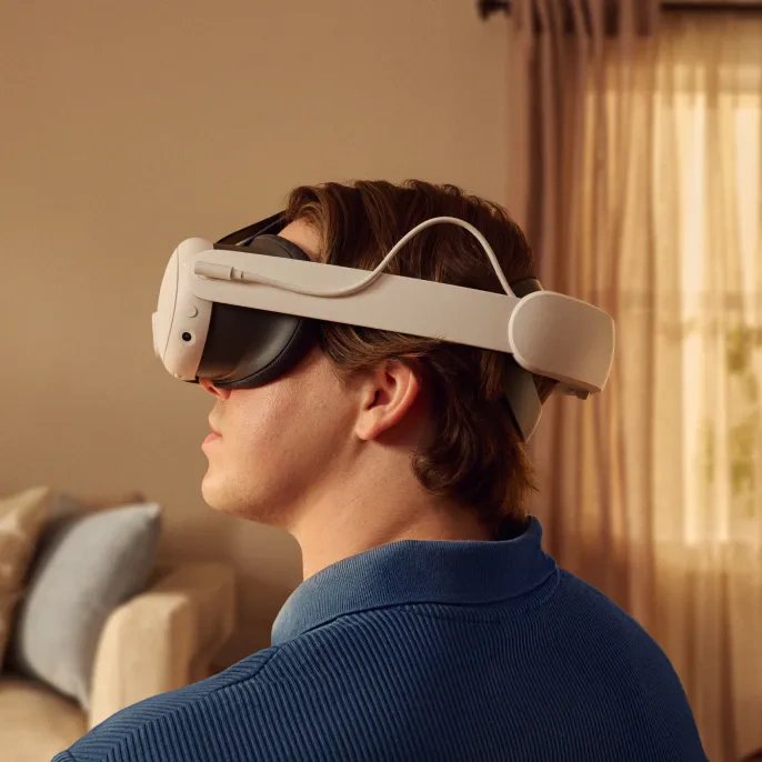 Eine Person, die ein VR-Headset von hinten trägt. Sie befinden sich in einem Raum mit einer Couch und Vorhängen. Das Headset ist weiß.