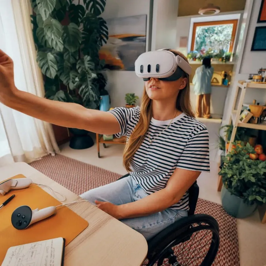 Donna con visore VR in sedia a rotelle, si protende. Scrivania con controller e blocco note. Piante e finestra sullo sfondo.