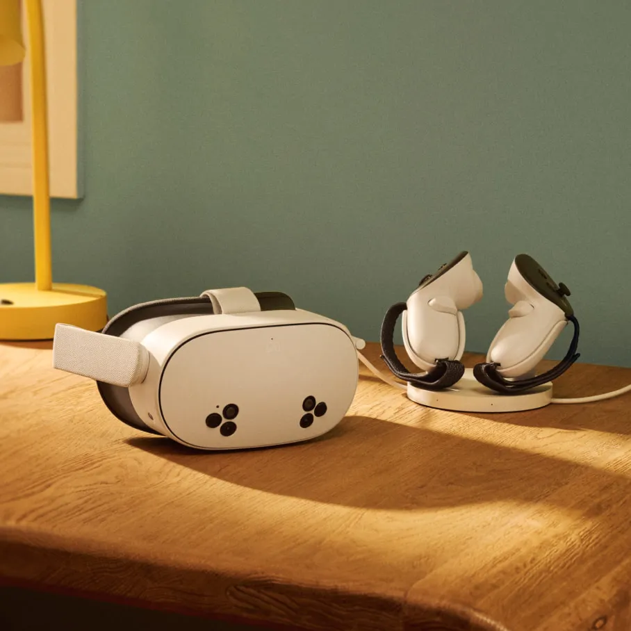 Un visore VR e dei controller sono su un tavolo di legno. Il visore è bianco e nero. I controller sono bianchi e su una base di ricarica.