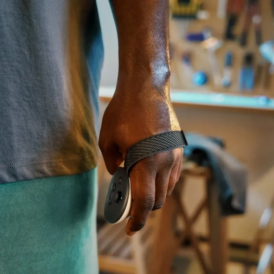 Die Hand einer Person hält ein kleines, schwarz-weißes kreisförmiges Gerät mit Knöpfen, das an einem Handgelenkband befestigt ist. Der Hintergrund ist unscharf.