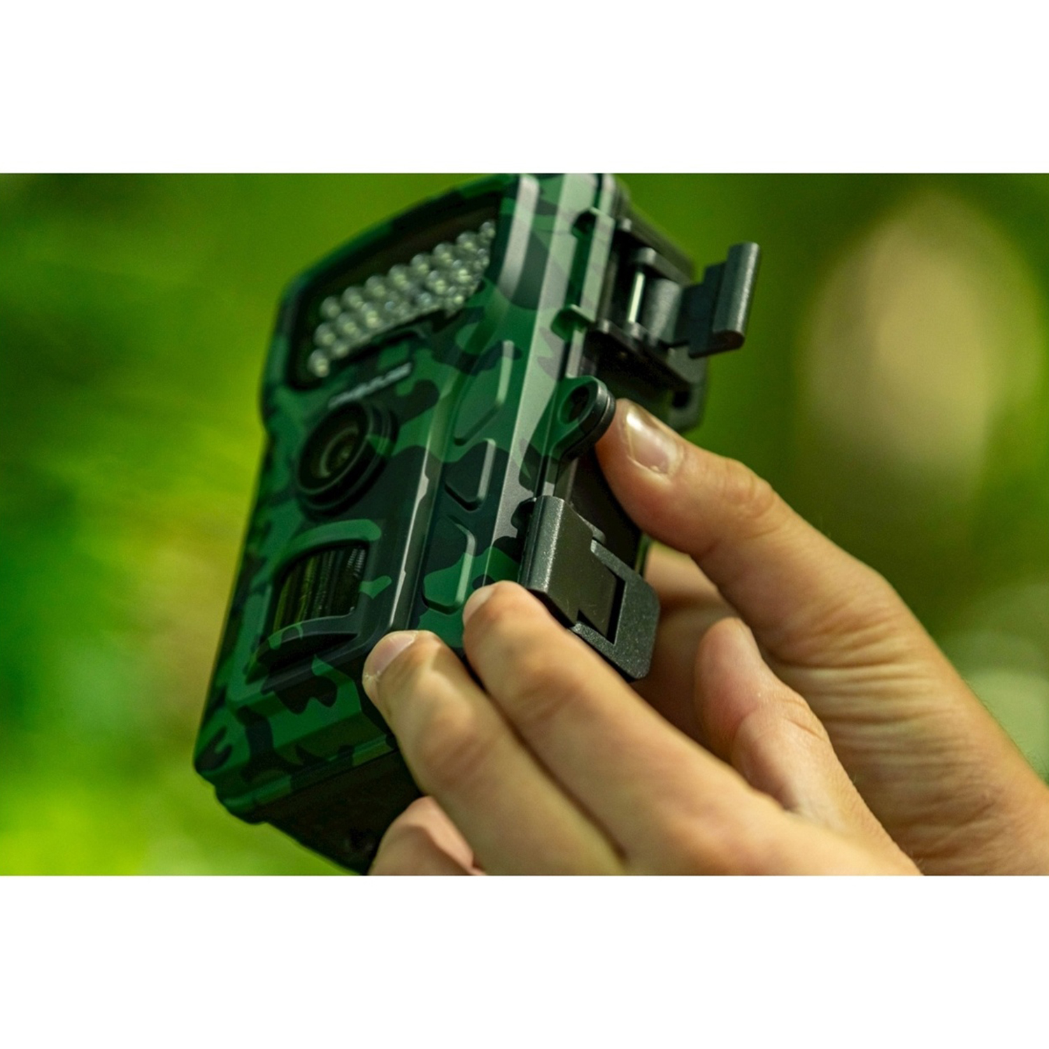 Le mani di una persona tengono una fotocamera mimetica verde. La fotocamera ha un obiettivo e luci a LED, con uno sfondo verde sfocato.