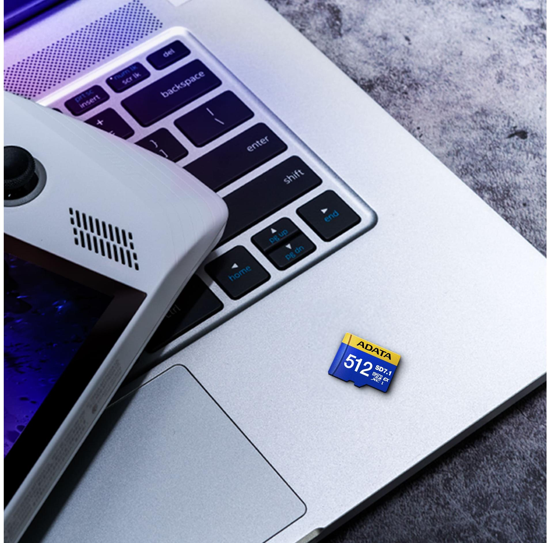Un clavier d'ordinateur portable et un appareil de jeu portable. Il y a une carte SD bleue sur l'ordinateur portable. La scène est sur une surface grise.
