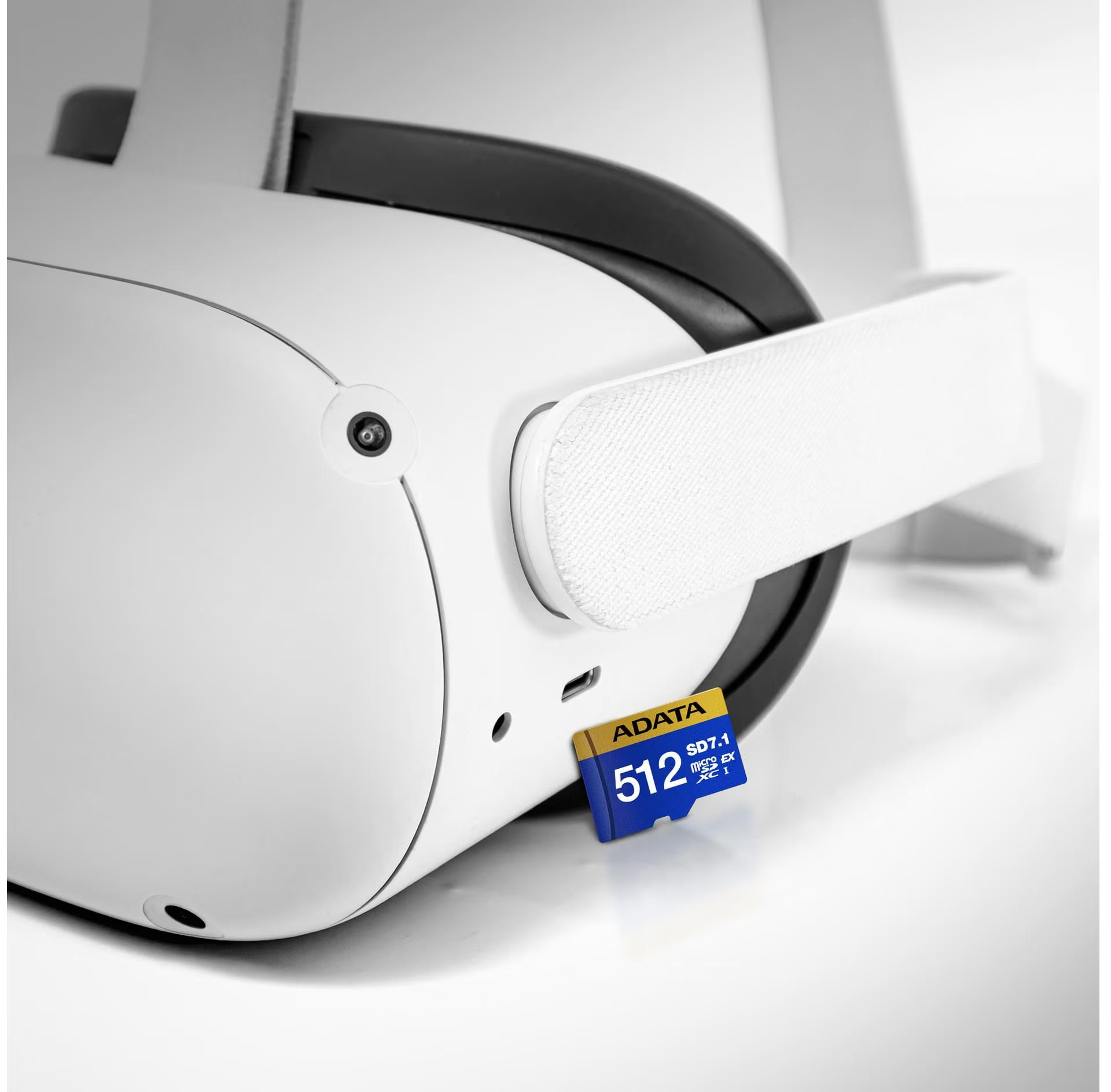 Un casque de réalité virtuelle avec une sangle blanche et une carte SD ADATA bleue et or insérée. Le casque est blanc et noir.