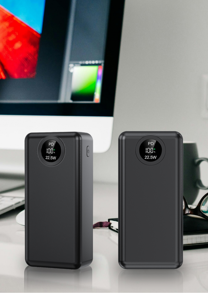Két fekete power bank az asztalon. A háttérben egy számítógép monitor, egy bögre és egy szemüveg látható.