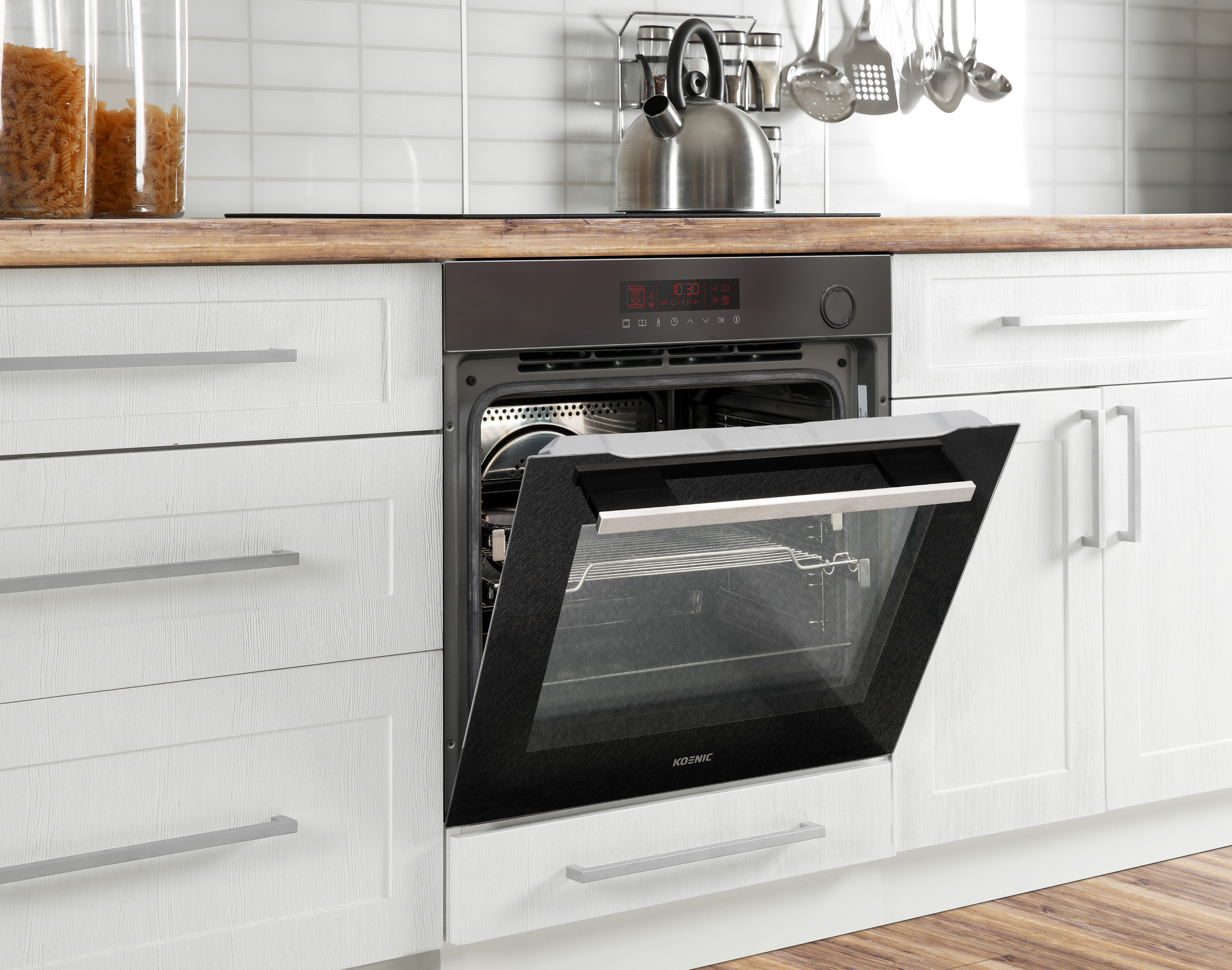 Kitchen scene with an open oven. White cabinets, stainless steel kettle, and pasta jars are visible.