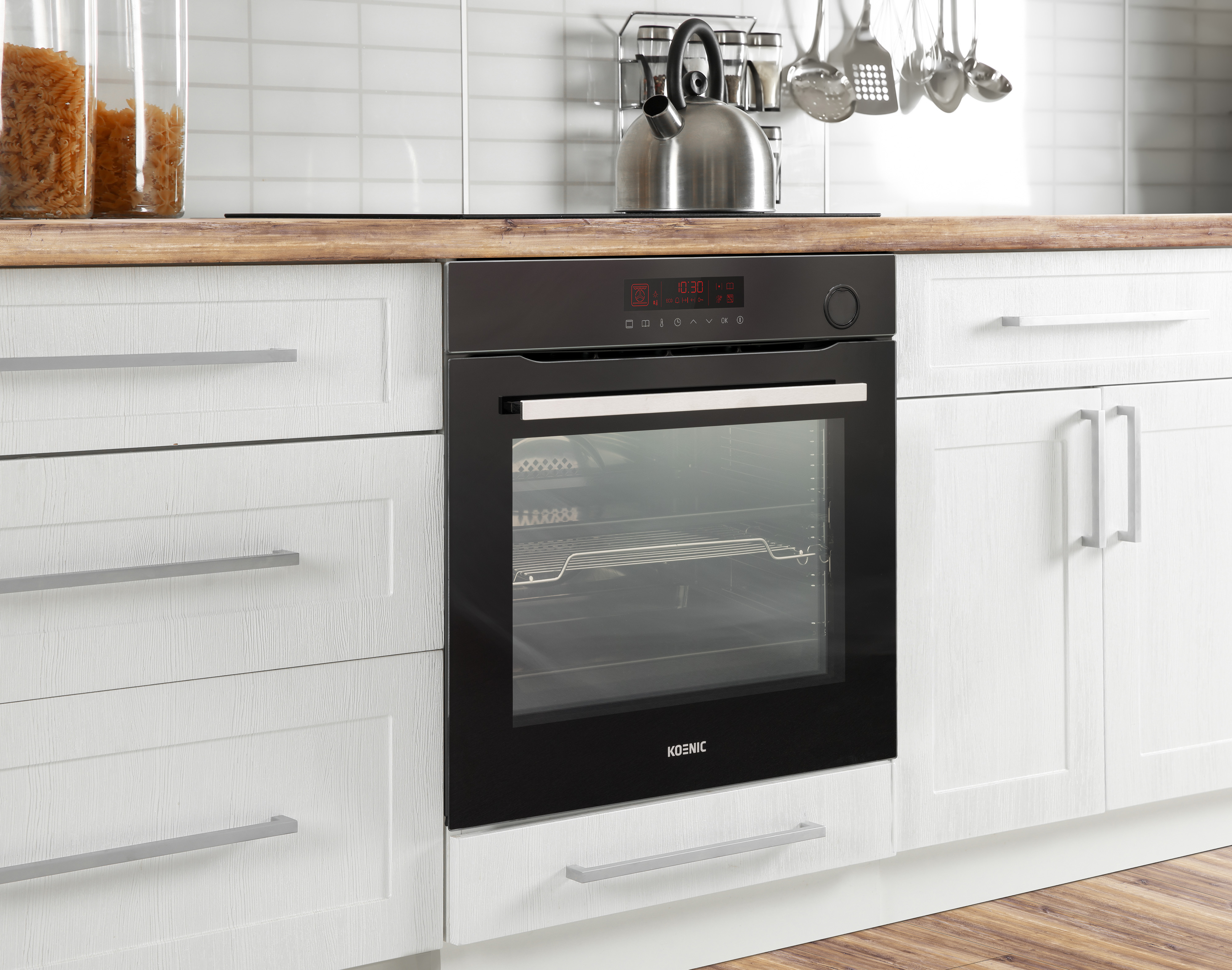 A kitchen scene with a black oven, white cabinets, and a wooden countertop. A kettle and utensils hang above.