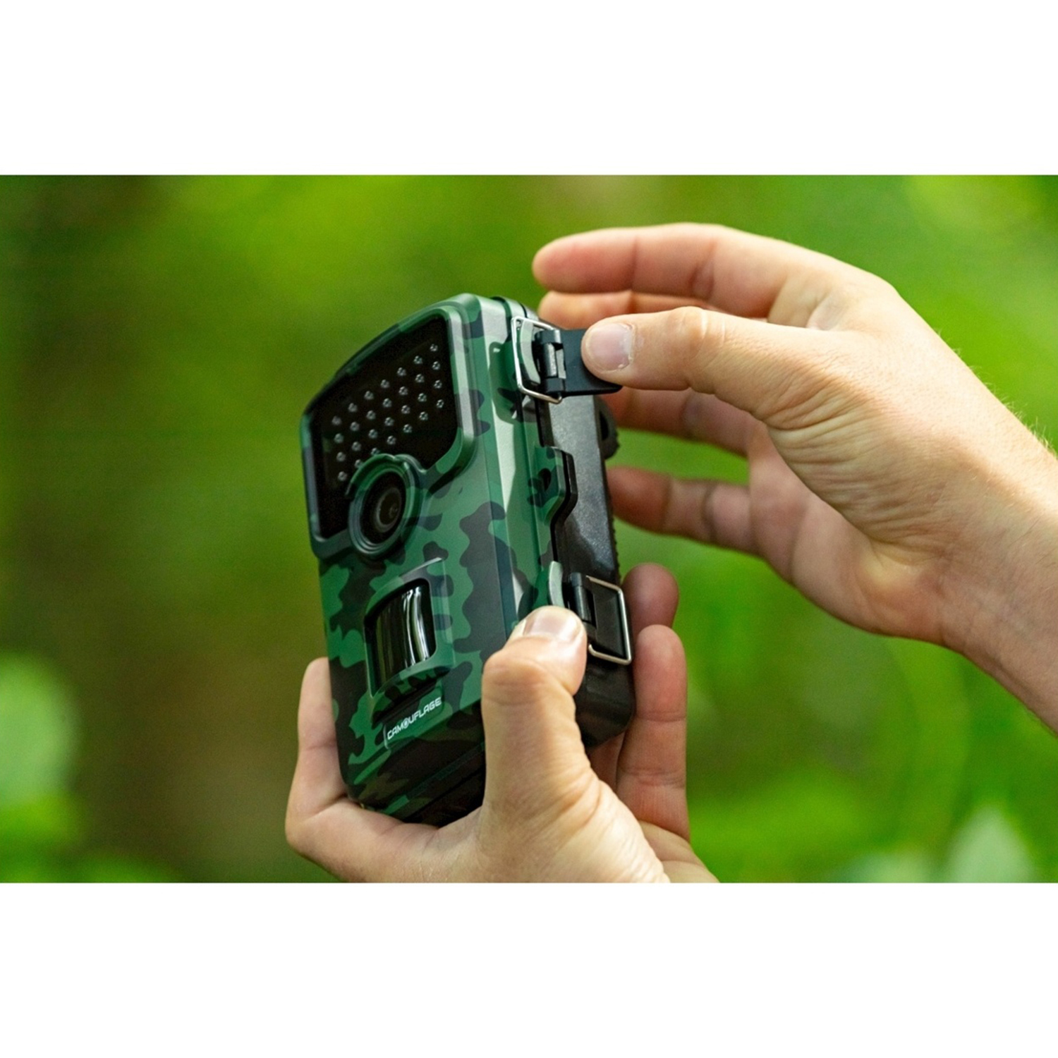 Mani che tengono una fotocamera mimetica verde. Lo sfondo è un fogliame verde sfocato.