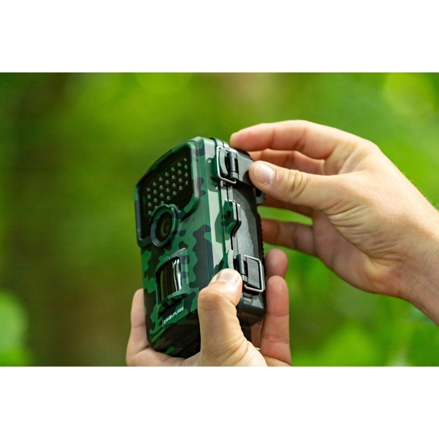 Mani che tengono una fotocamera mimetica su uno sfondo verde sfocato di fogliame. La fotocamera è nera e verde.