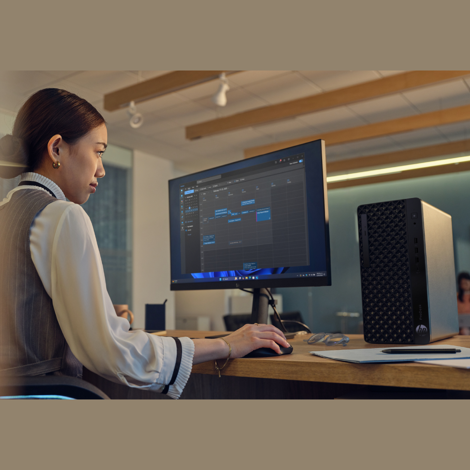 Woman using a computer, with a calendar on the screen, and a desktop computer on the right side.