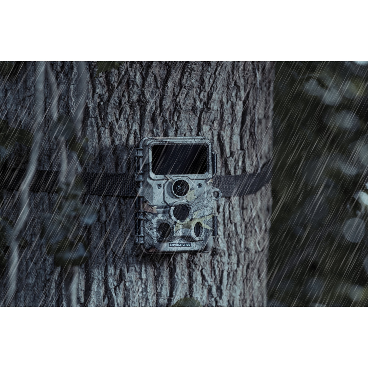 Una fotocamera da caccia mimetica è montata su un tronco d'albero, fissata con una cinghia nera. La pioggia cade sullo sfondo, sfocando la scena.