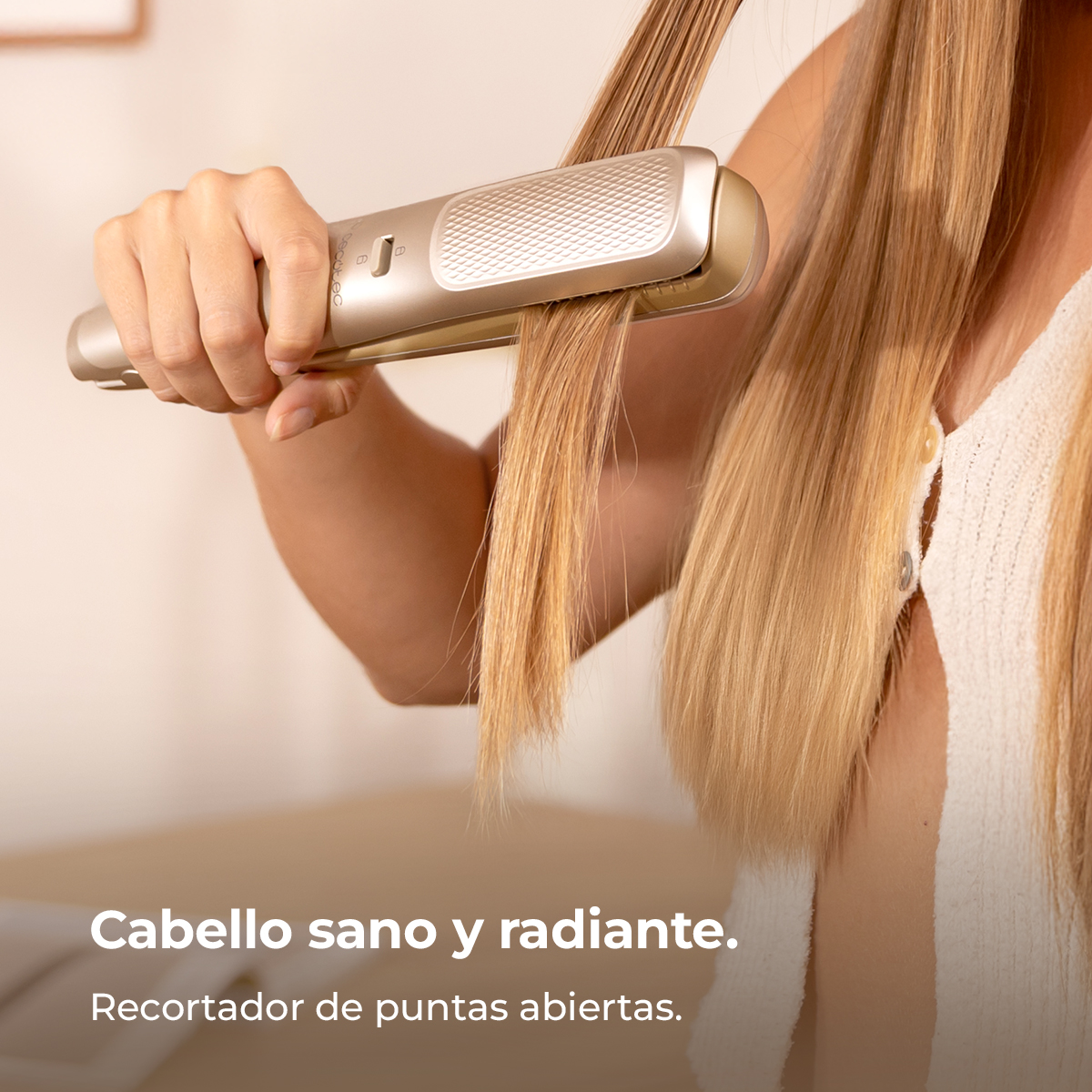 Una persona usa una plancha para el cabello en cabello largo y rubio. La plancha es dorada. El fondo es de color crema neutro.