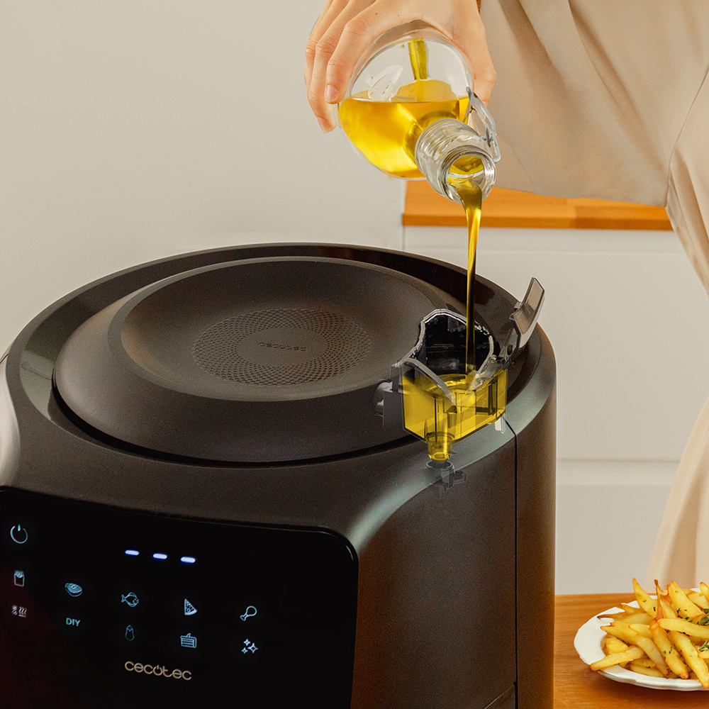 Una persona vierte aceite de una botella de vidrio en una freidora de aire. Papas fritas en un plato en el fondo.