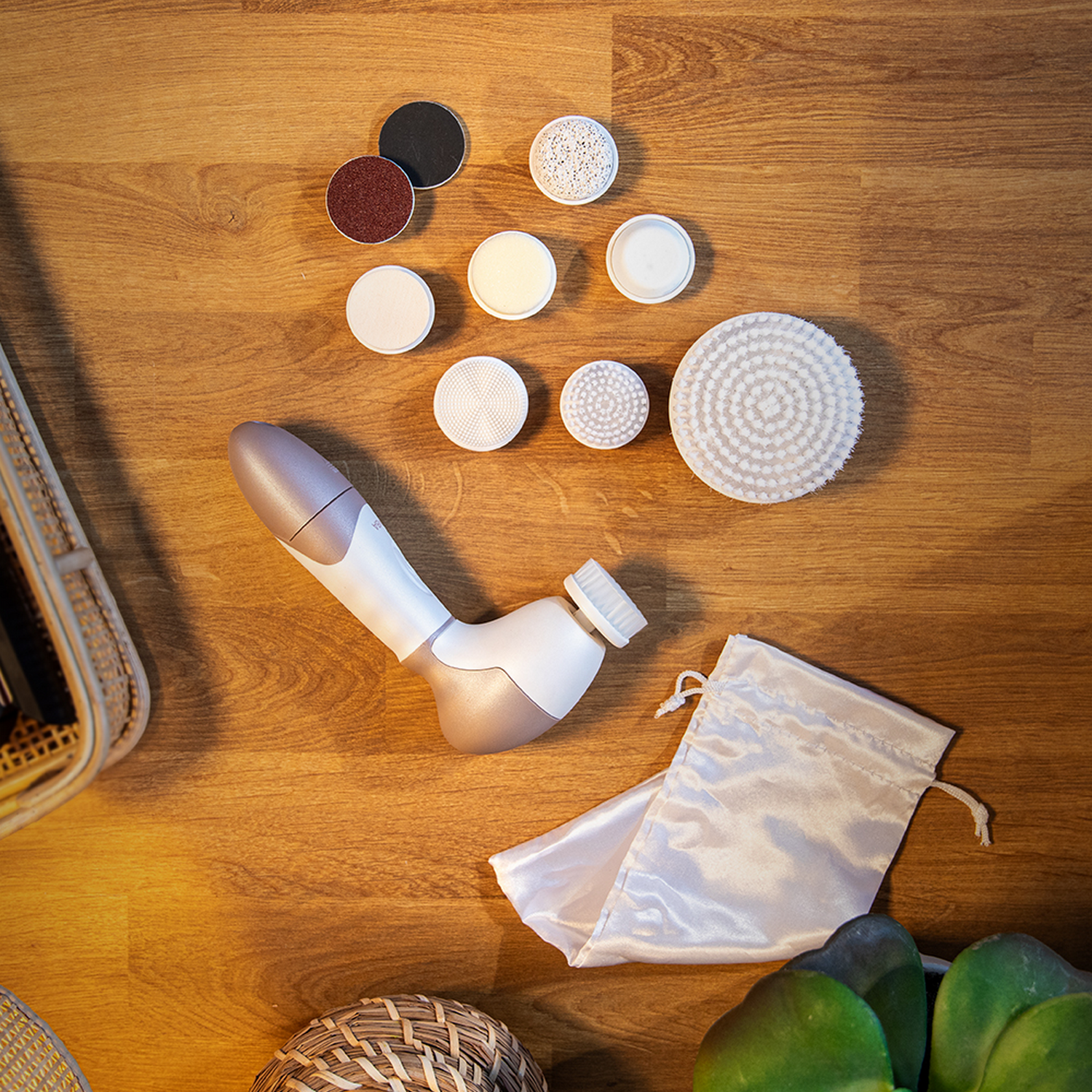 Un dispositivo para el cuidado de la piel con varios cabezales y accesorios descansa sobre una superficie de madera. Una bolsa de satén blanco está cerca.