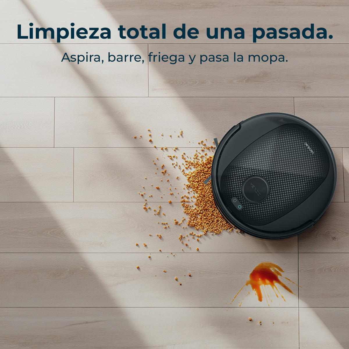 Un robot aspirador negro en un suelo de madera. Está limpiando granos derramados y una mancha.