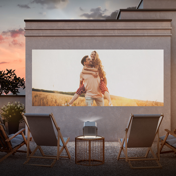 Pareja en pantalla, cine al aire libre con sillas y proyector. Cielo al atardecer al fondo.