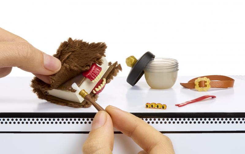 Eine Hand hält ein Spielzeugbuch mit Zähnen und einem kleinen Pinsel. Weitere Spielzeuge sind ein Glas, ein Gürtel und kleine gelbe Objekte.