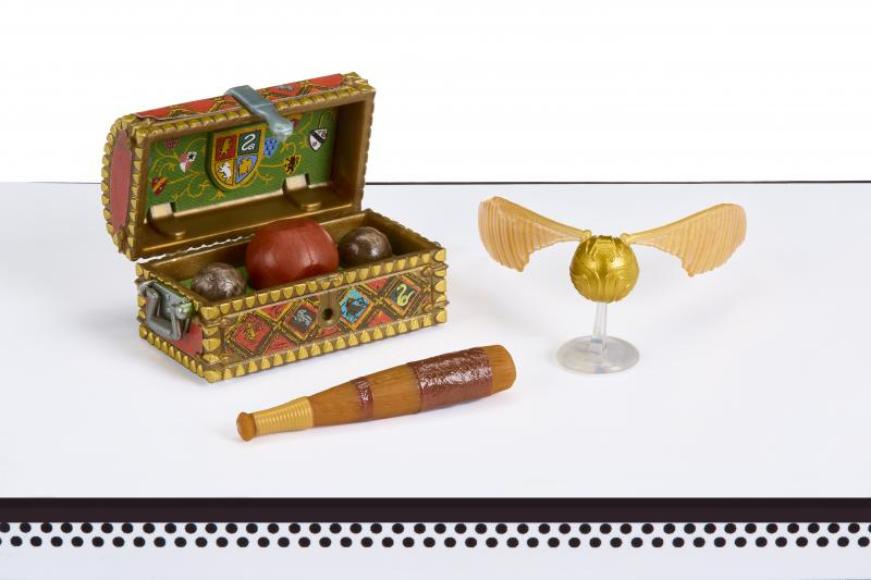 Eine Truhe mit Bällen, ein Schläger und ein goldener Schnatz. Die Truhe ist offen, der Schnatz steht auf einem durchsichtigen Ständer, alles auf weißem Untergrund.