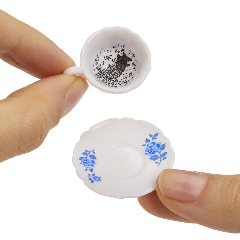 Eine Miniatur-Teetasse, die über einer Untertasse gehalten wird. Beide sind weiß mit blauen Blumenmustern. Das Innere der Teetasse hat ein schwarzes Muster.