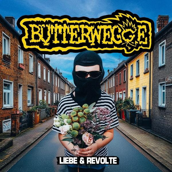 Person in schwarzer Sturmhaube und Sonnenbrille hält Blumen auf der Straße. Gebäude säumen den Hintergrund.