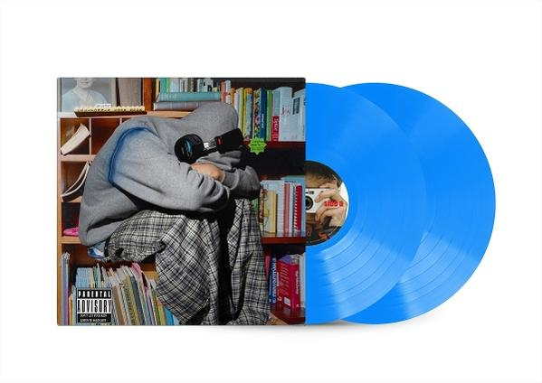 Eine Person mit Kapuzenpullover sitzt vor einem Bücherregal mit blauen Schallplatten. Die Person trägt Kopfhörer.
