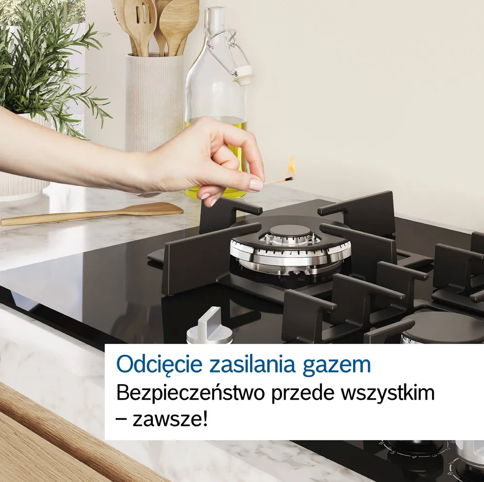 Ręka trzyma zapaloną zapałkę nad czarną kuchenką gazową. Tło pokazuje przedmioty kuchenne.