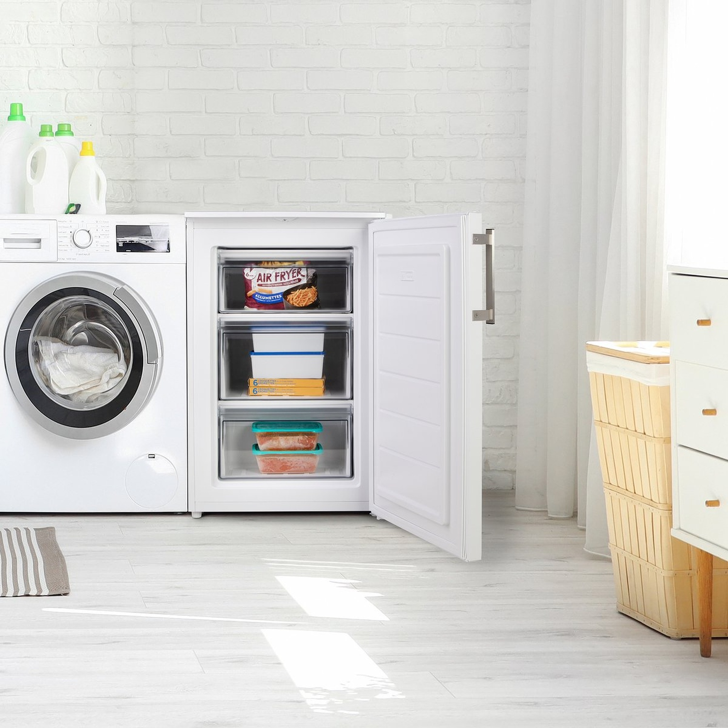 Un congélateur blanc avec la porte ouverte est à côté d'une machine à laver. À l'intérieur du congélateur, il y a des récipients alimentaires. À gauche, une machine à laver.