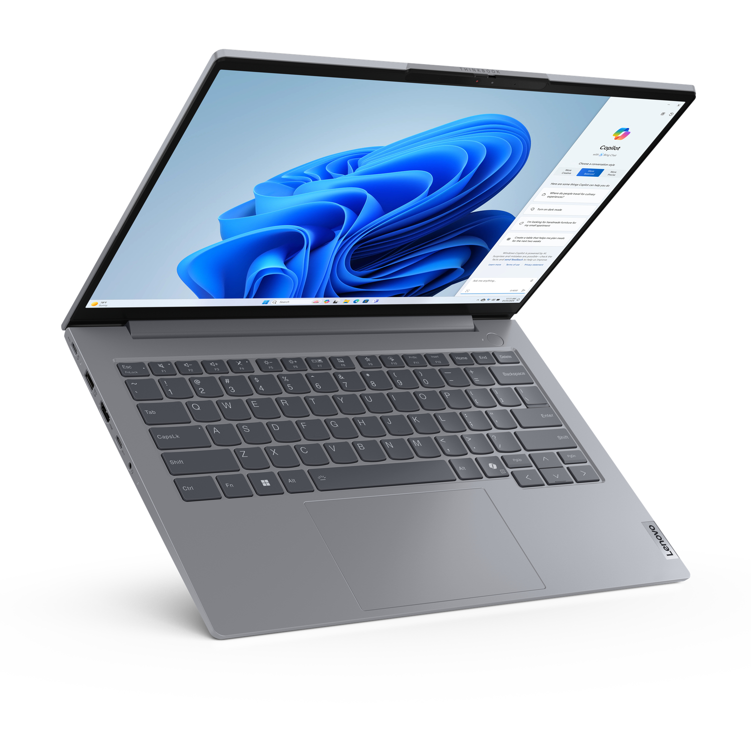 A grey Lenovo laptop is open, showing a blue abstract wallpaper and the Windows 11 interface. The keyboard is visible.
