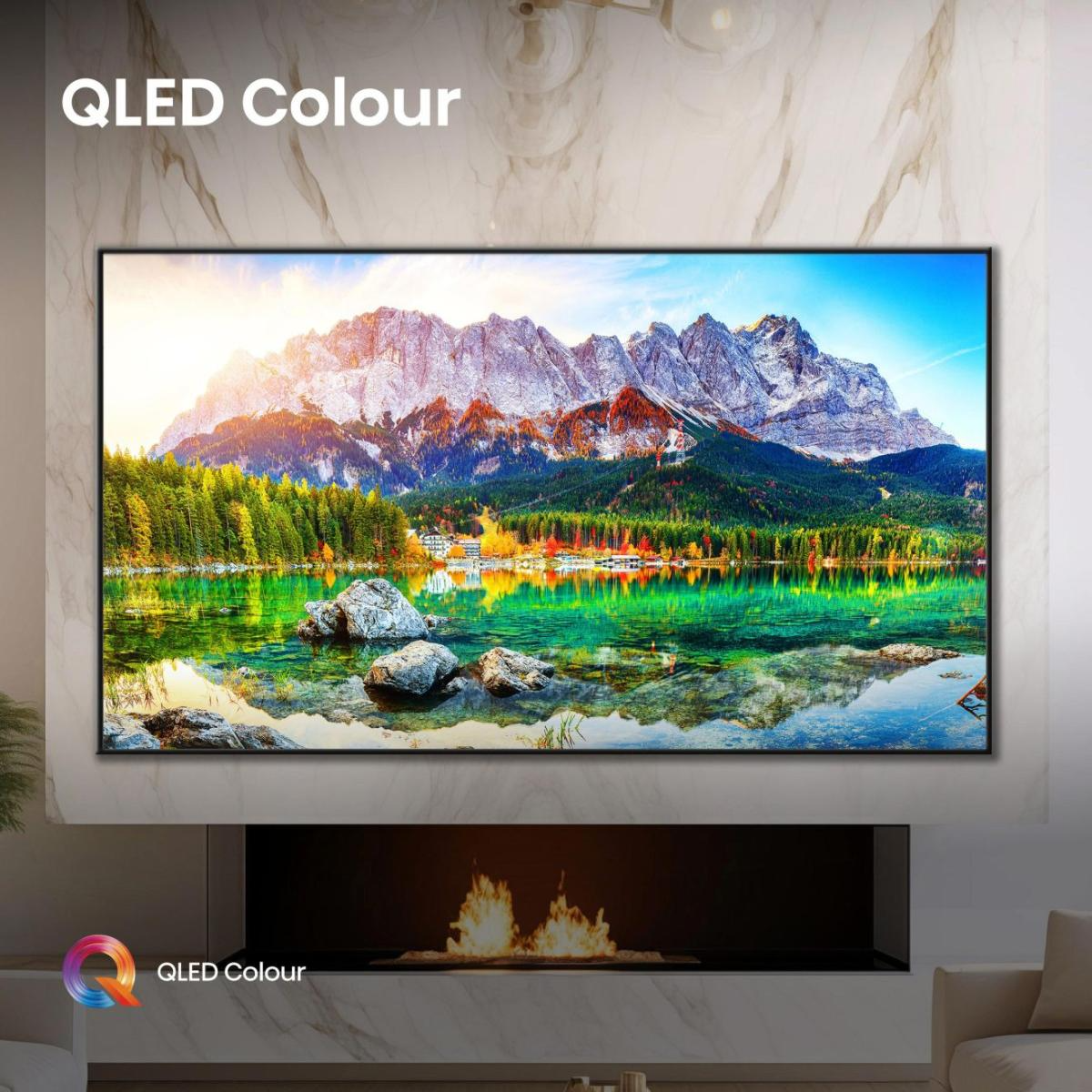 Egy QLED TV egy hegyvonulat festői kilátását jeleníti meg, amely egy tóban tükröződik. A TV alatt egy kandalló található.