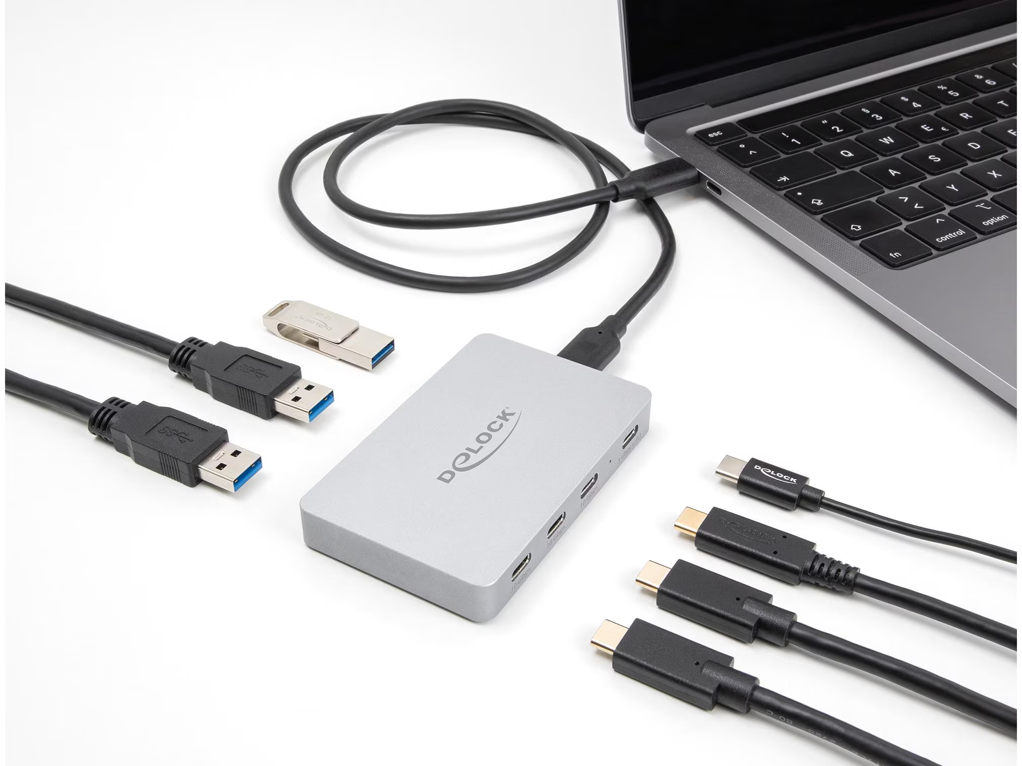 Un ordinateur portable connecté à un hub gris avec divers câbles USB et une clé USB. Tous les éléments sont posés sur une surface blanche.