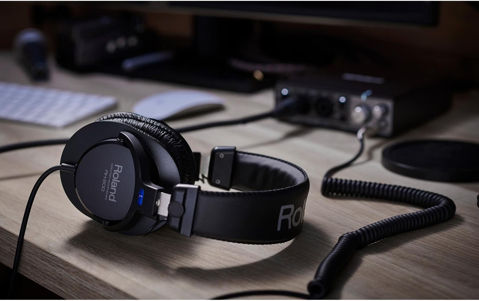 Schwarze Roland-Kopfhörer auf einem Holztisch mit einem Soundinterface und Computerzubehör im Hintergrund.
