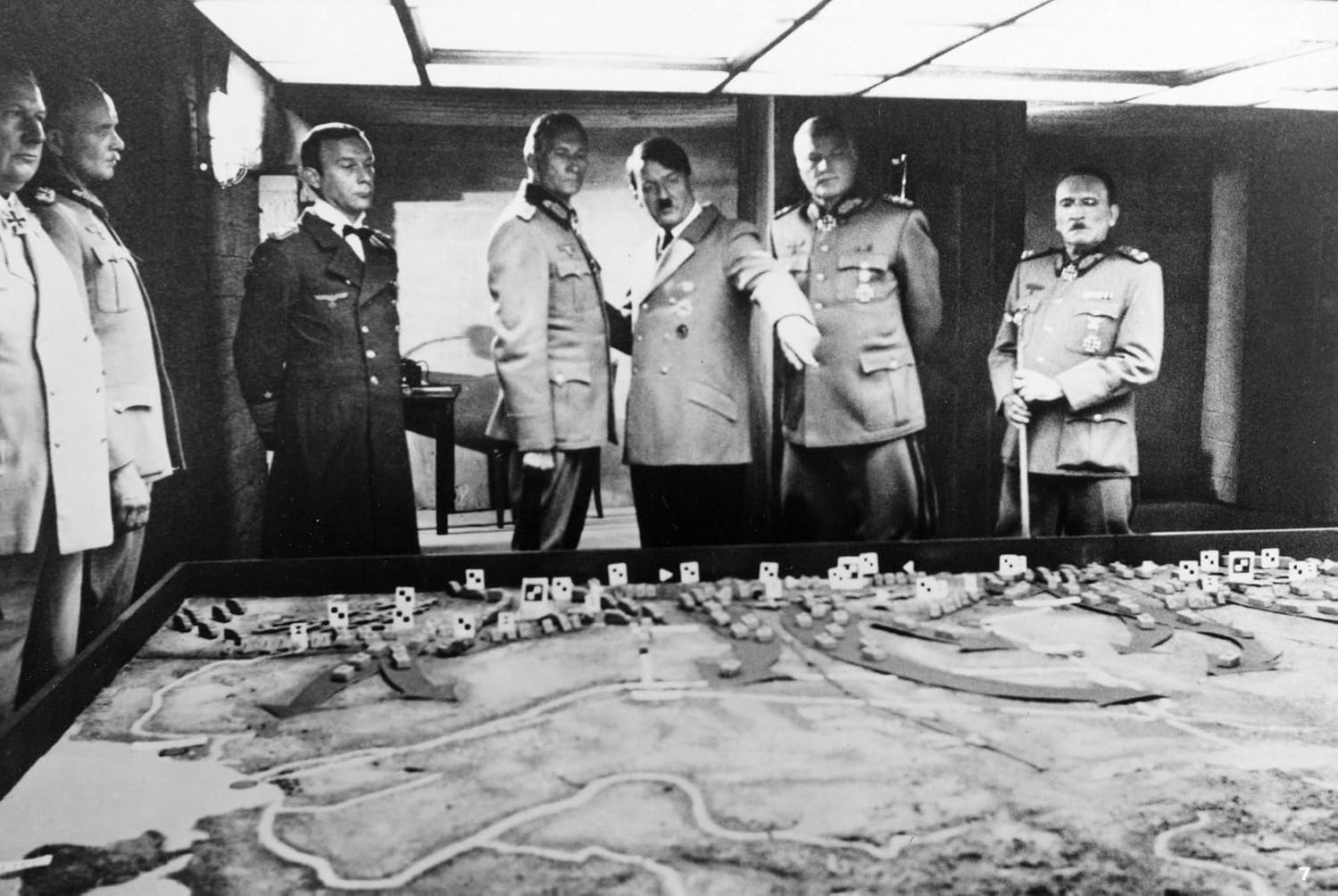 Männer in Militäruniformen stehen um einen Tisch mit einer detaillierten Karte. Ein Mann im Anzug zeigt auf die Karte.