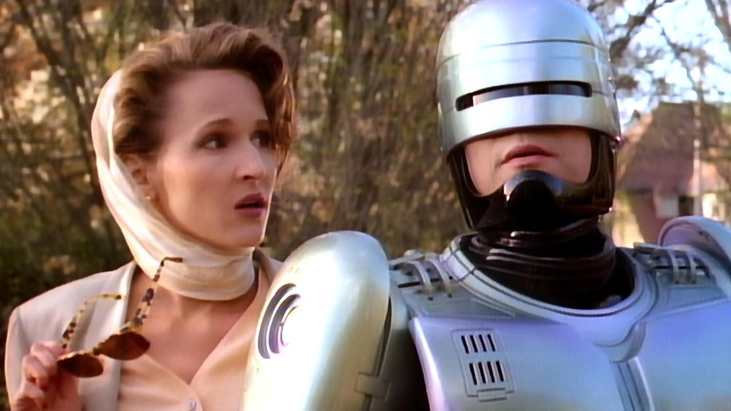 Eine Frau mit Kopftuch blickt Robocop an, der sich auf der rechten Seite des Bildes befindet, in einer sonnigen Umgebung im Freien.
