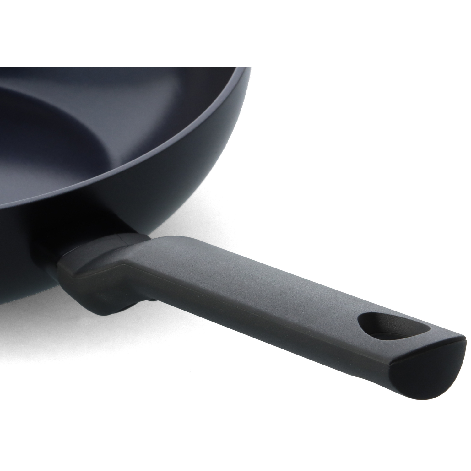 Close-up of a dark gray frying pan with a black handle. The handle has a hole at the end. The pan is on a white surface.