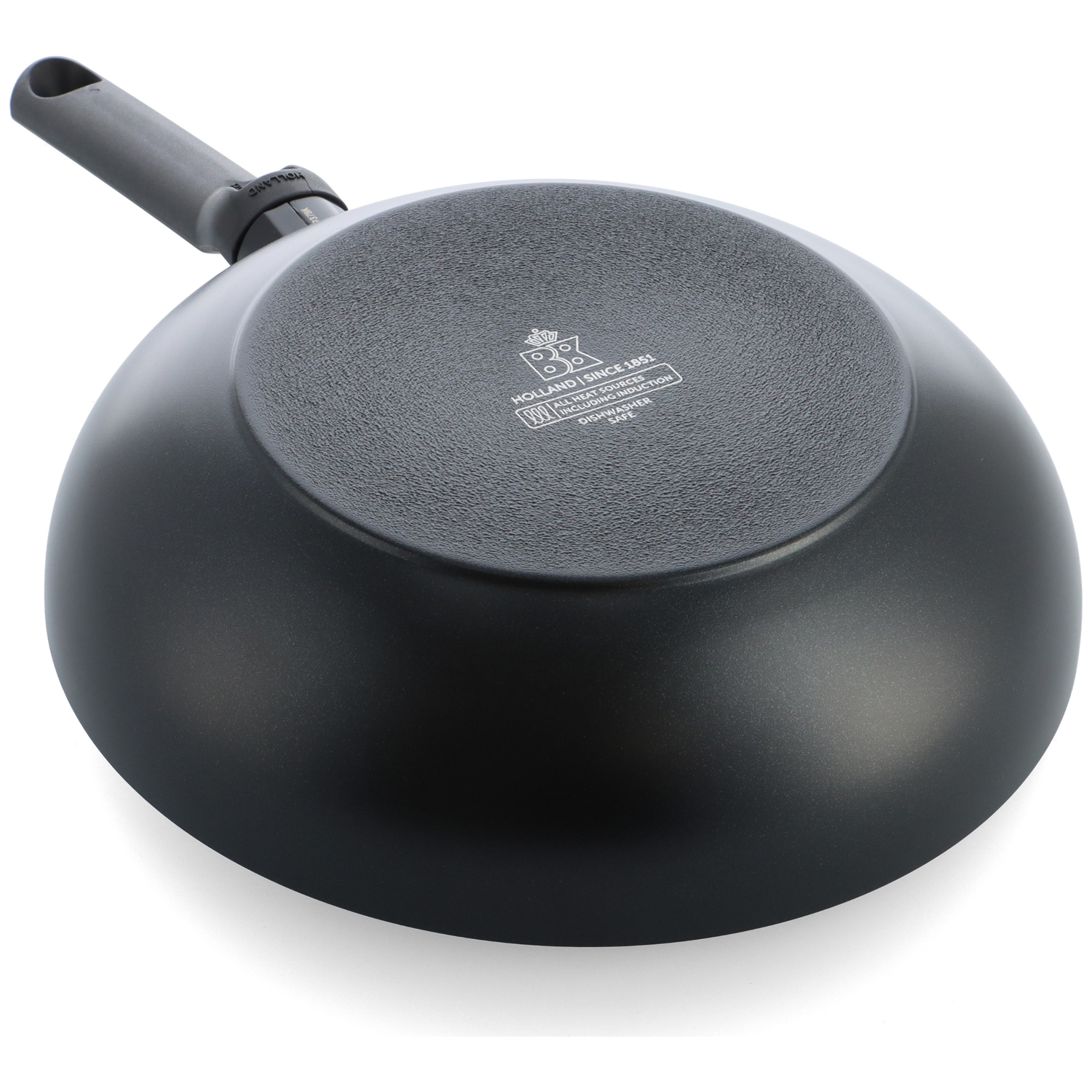 The bottom of a black wok on a white surface. The handle is gray. The wok has text and a logo on the bottom.