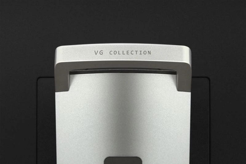 Közelkép egy ezüst fogantyúról, rajta a 'VG COLLECTION' felirattal. A fogantyú ezüst felületen, fekete háttér előtt látható.