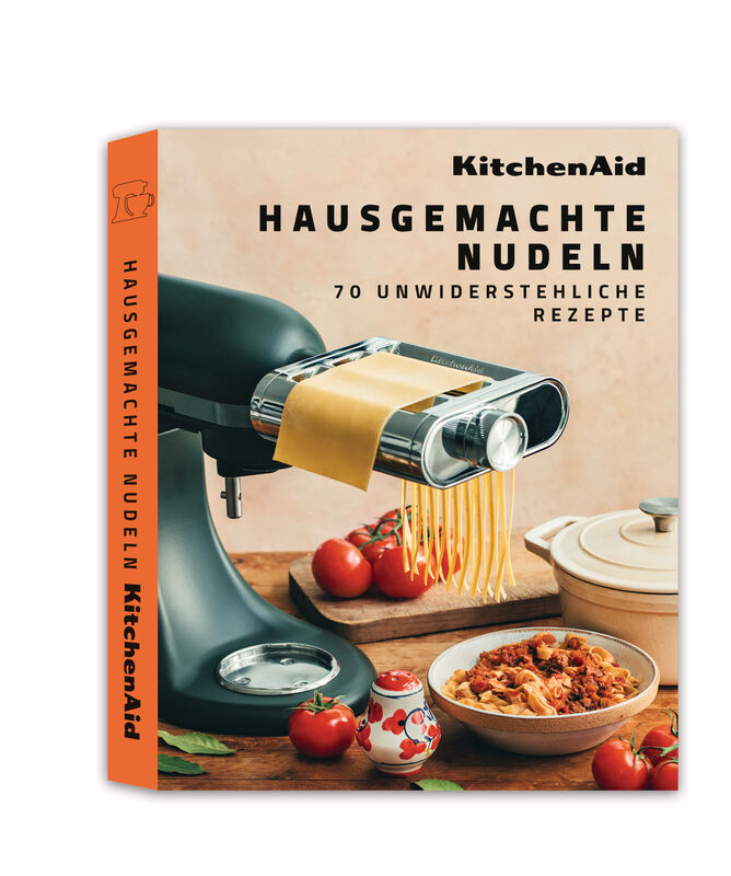 Ein KitchenAid-Kochbuch mit dem Titel "Hausgemachte Nudeln". Mit einer Maschine wird Pasta hergestellt. Tomaten, Nudeln und ein Topf sind sichtbar.