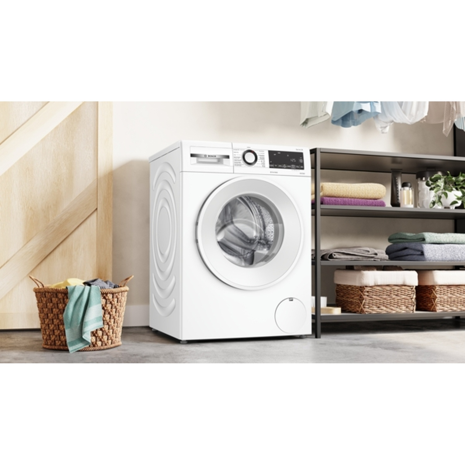 Een witte wasmachine staat naast een houten deur en een wasmand. Planken houden handdoeken en planten vast.