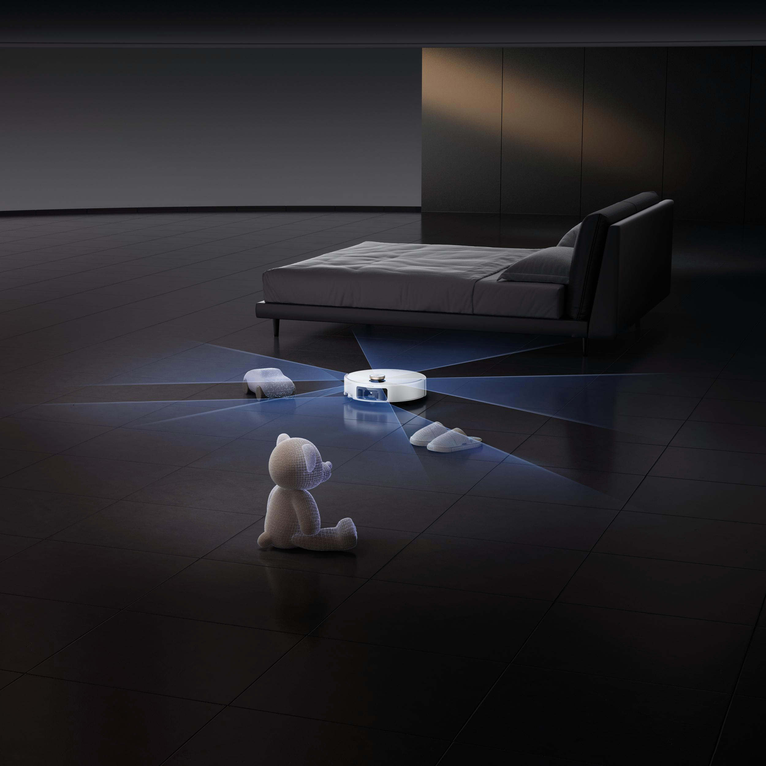 Ein Roboter-Staubsauger scannt einen Raum mit Bett, Hausschuhen und Teddybär. Der Boden ist dunkel gefliest.