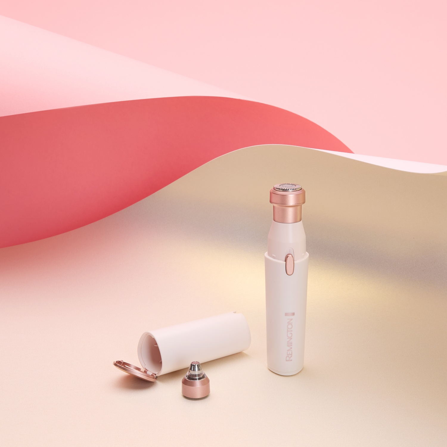 A white and rose gold Remington epilator with parts scattered on a surface with pink and beige paper folds.