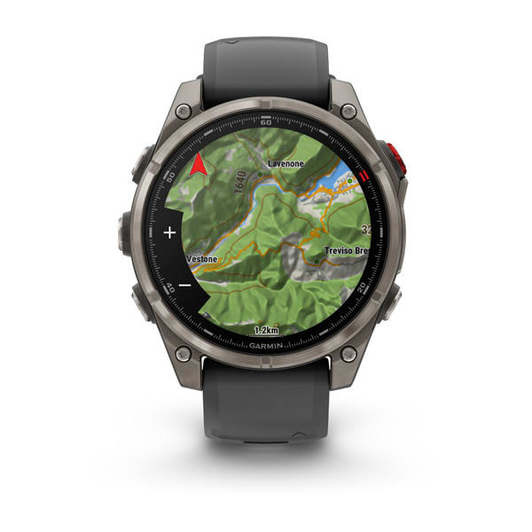 Egy Garmin okosóra egy hegyvidéki terület térképét jeleníti meg. Az óra szürke, fekete képernyővel és piros gombbal. Az óraszíj szürke.