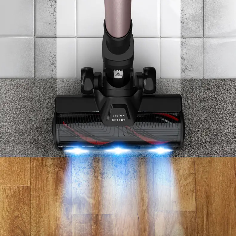 Czarna głowica odkurzacza czyszcząca różne powierzchnie: płytki, dywan i drewno. Niebieskie światła oświetlają drewnianą podłogę.