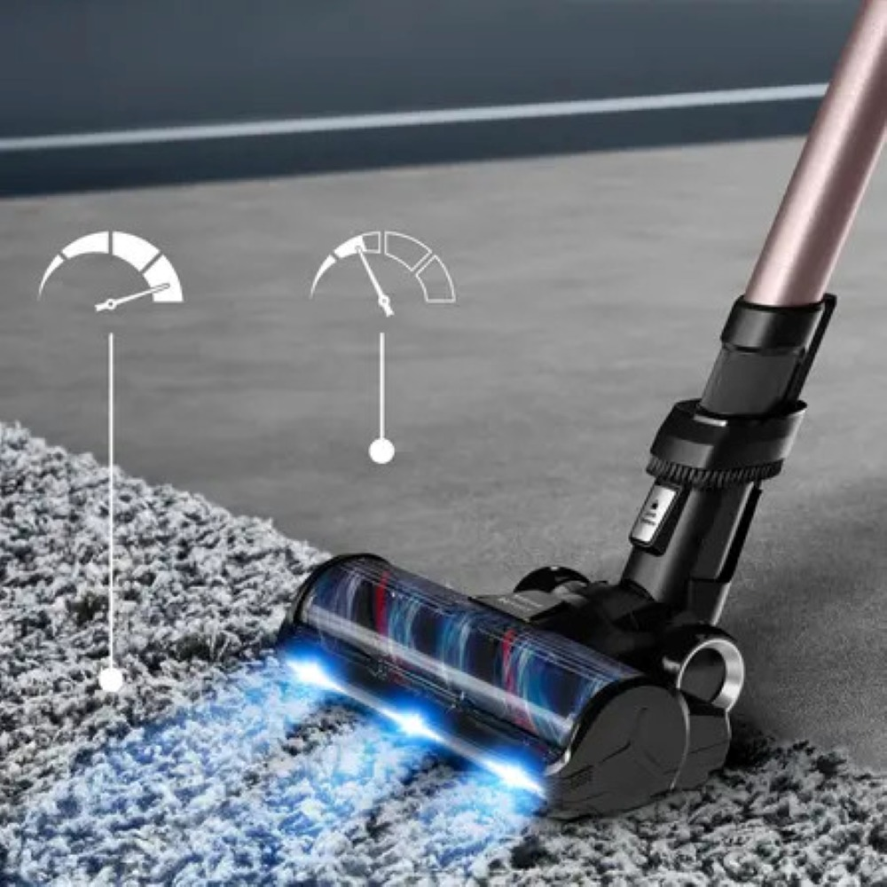 Odkurzacz czyszczący dywan. Odkurzacz ma różowo-złotą rurę i czarną głowicę. W tle znajdują się dwa wskaźniki prędkości.