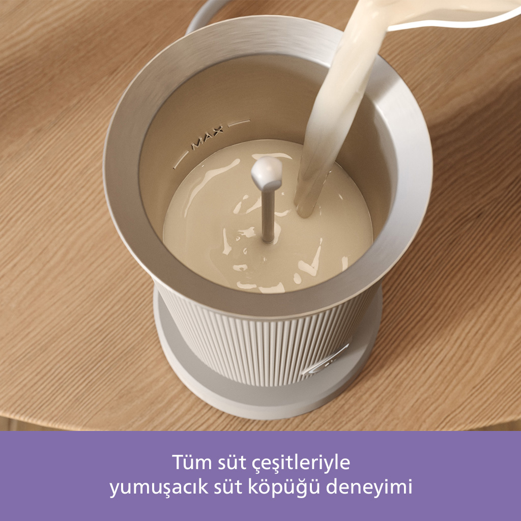 Süt, süt köpürtücüye dökülüyor. Köpürtücü gri ve beyaz renkte, ahşap bir yüzeyde duruyor. Süt açık renkli.