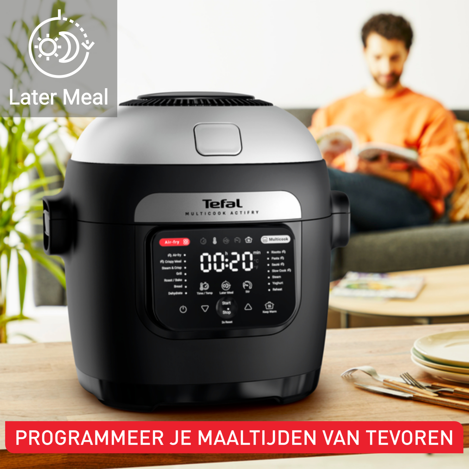 Een zwarte Tefal Multicook Actifry op een houten oppervlak. Een man leest op de achtergrond. Het display toont 00:20. Tekst: 'Later Meal'.