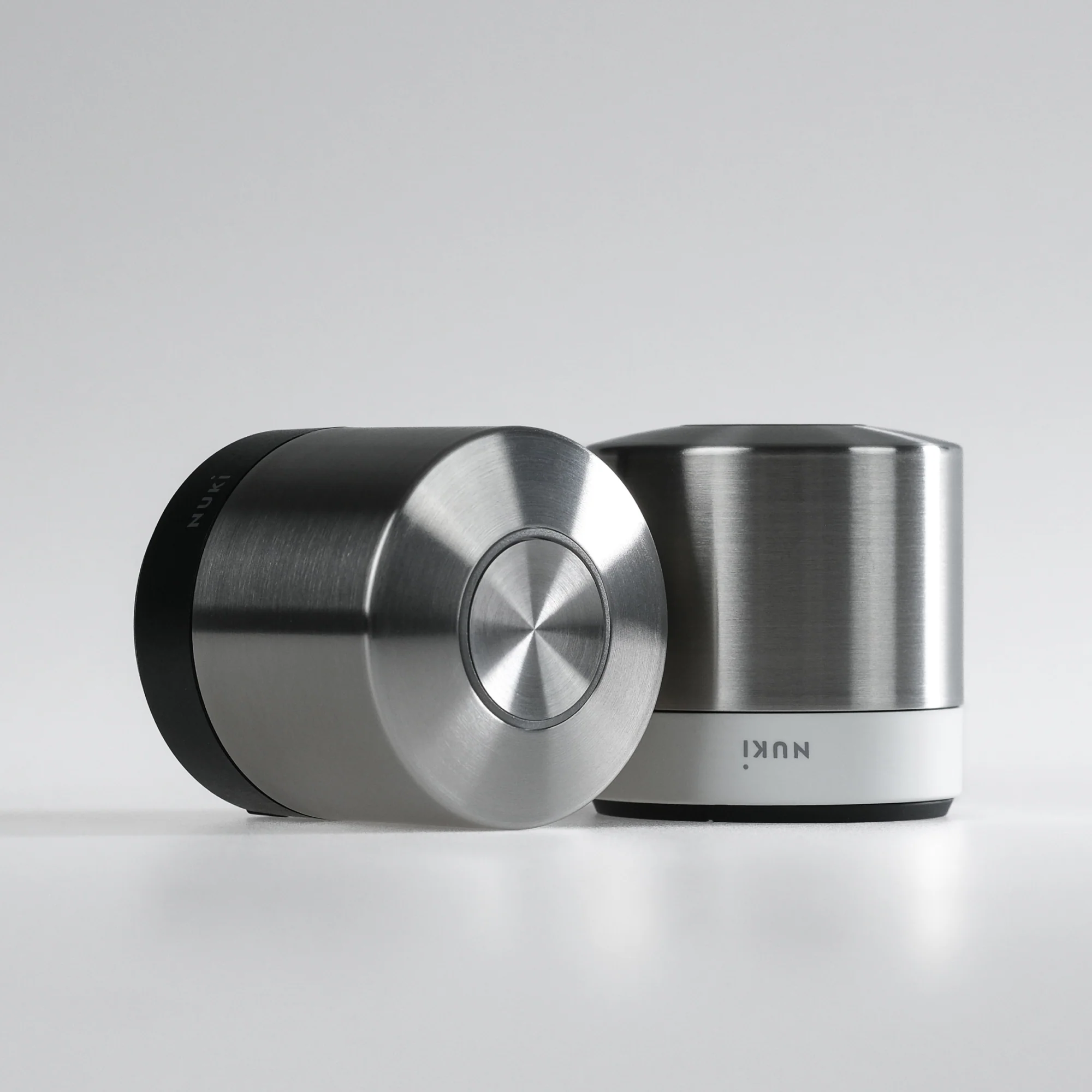 Zwei silberne Nuki Smart Locks. Eines links, teilweise sichtbar. Das andere rechts. Weißer Hintergrund.