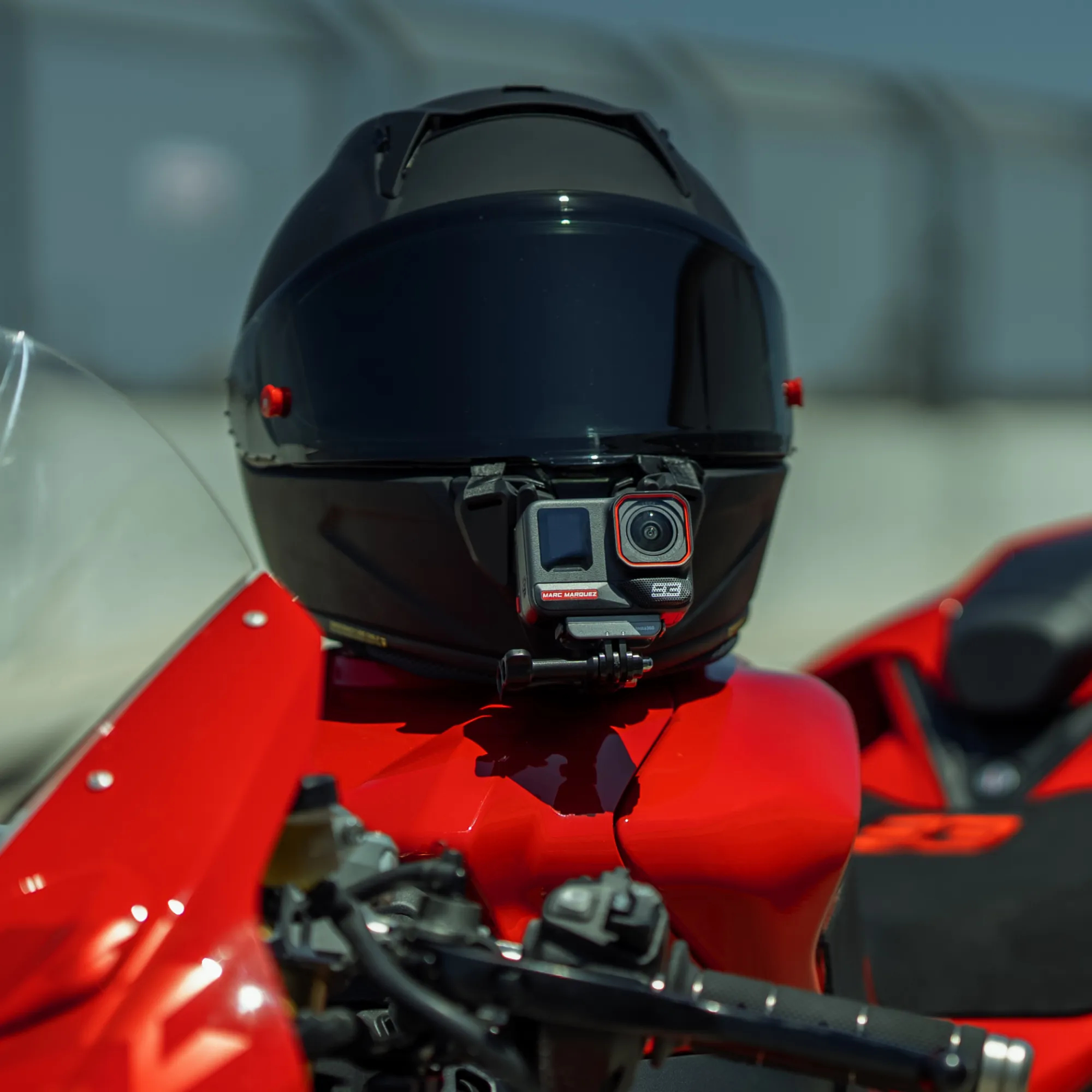 Schwarzer Motorradhelm mit Kamera, auf rotem Motorrad. Helle, sonnige Szene im Freien.
