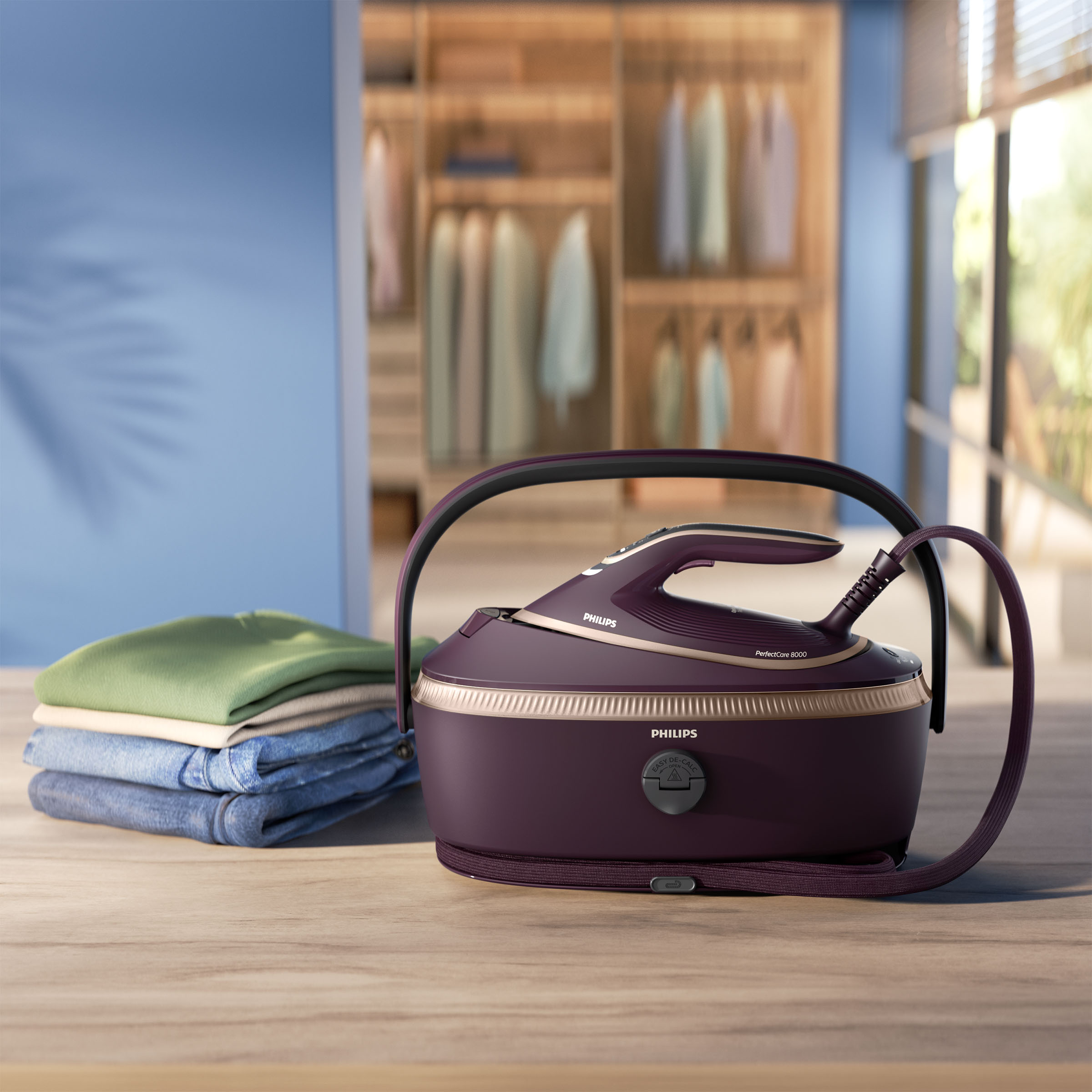 Fioletowe żelazko Philips, stos ubrań i szafa w tle.